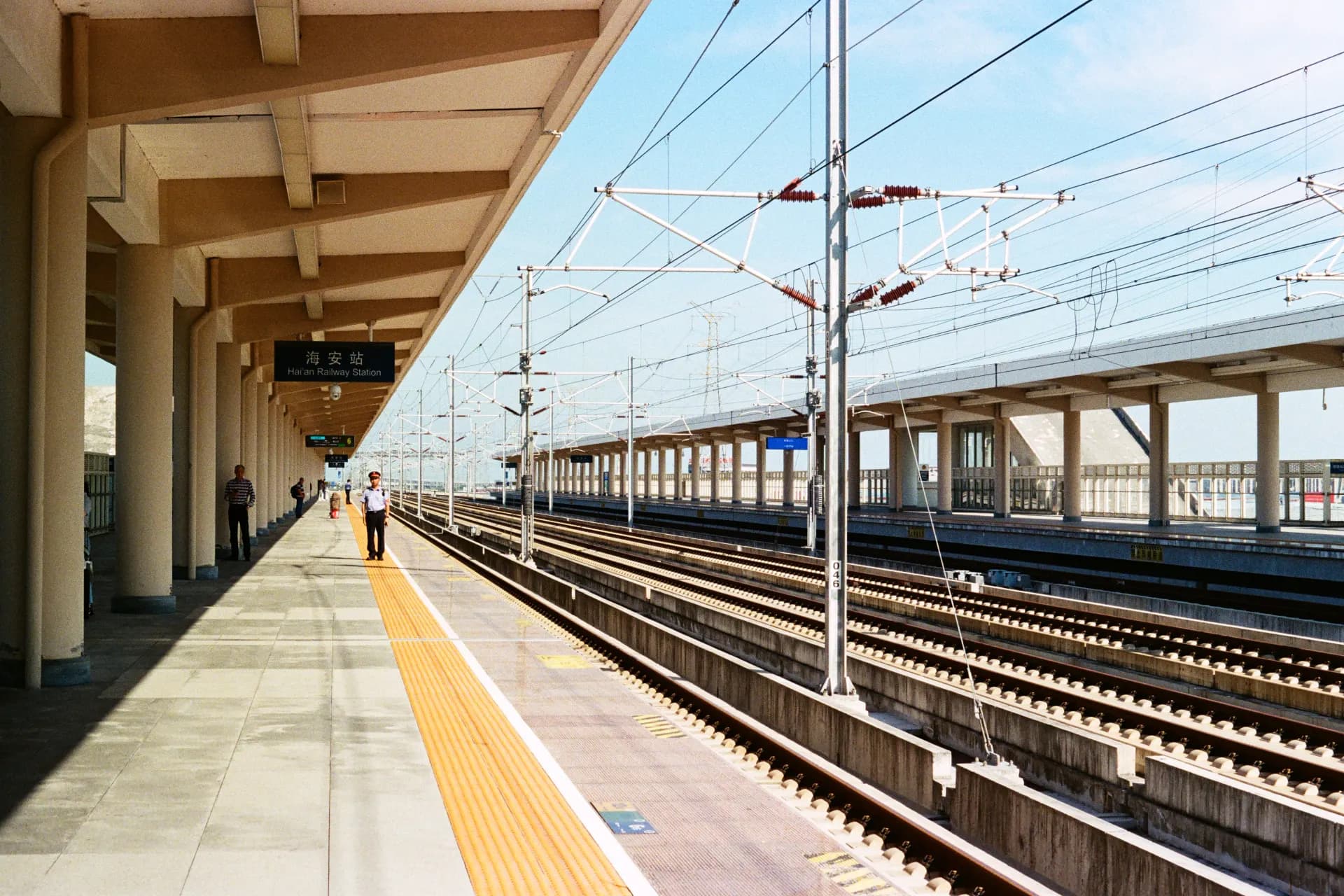 A train station platform with tracks and overhead wires.