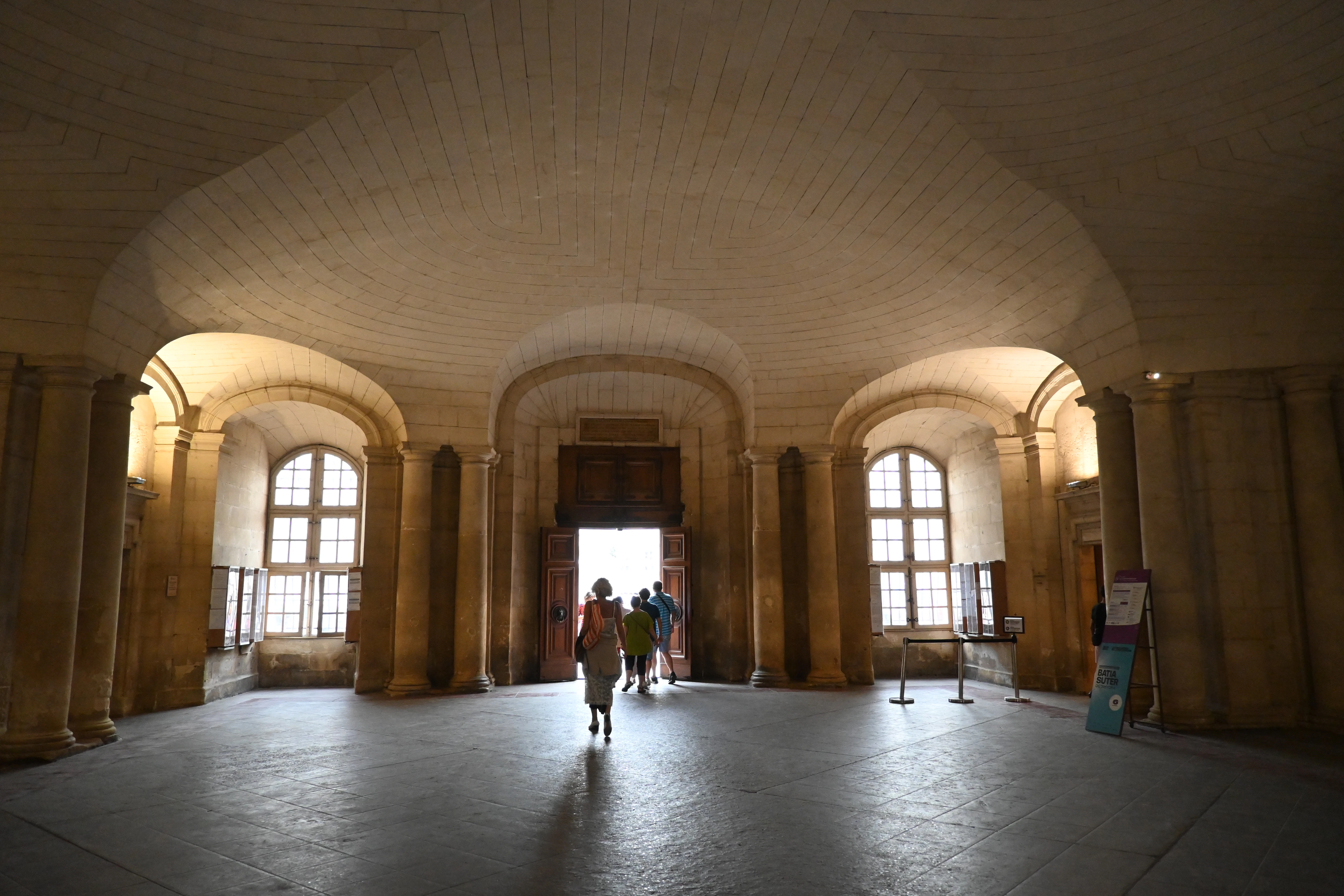 People walk through a grand hall with arched windows.