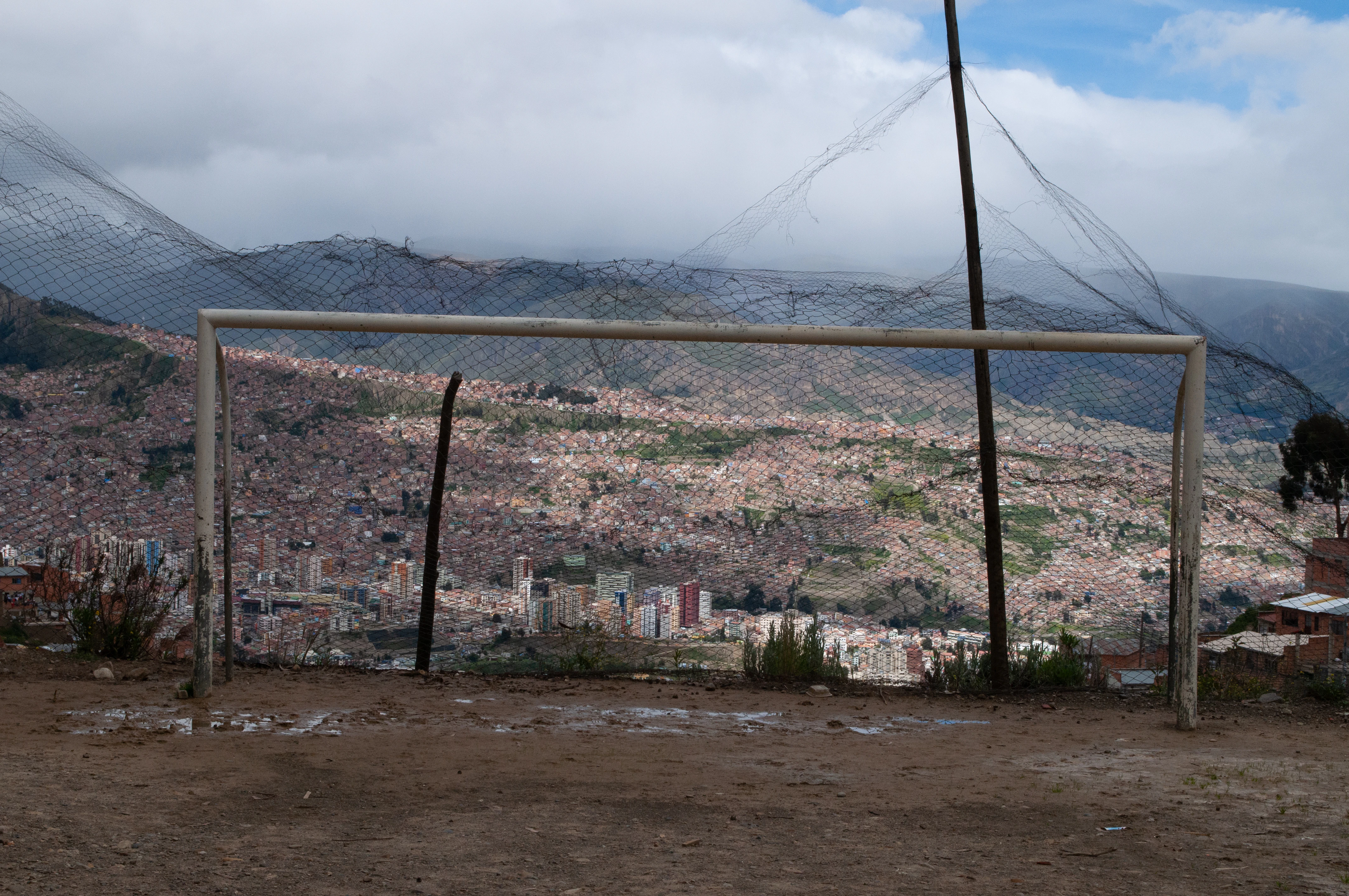 a soccer goal on a dirt field with a city in the background