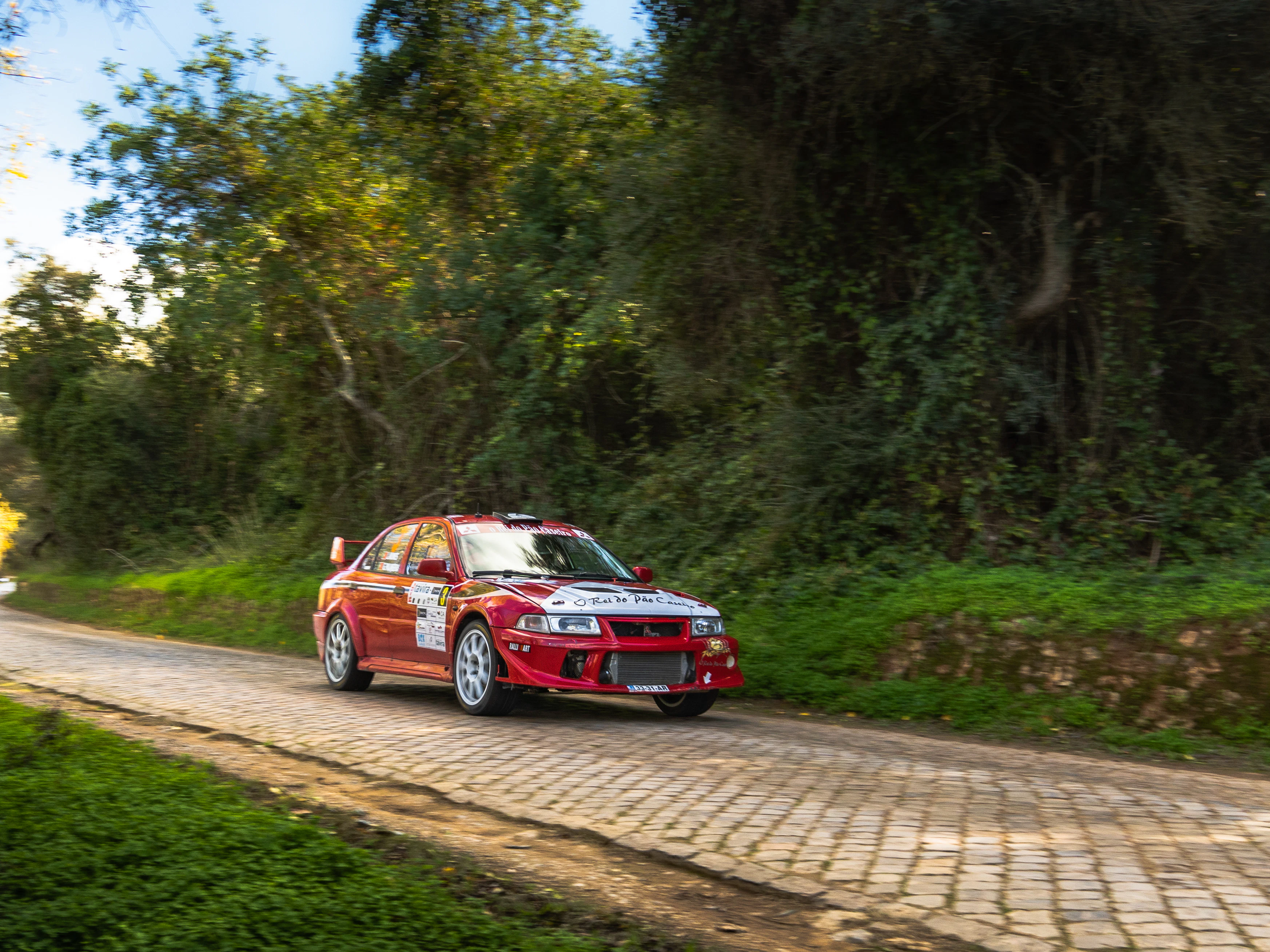 A red rally car drives on a paved road.