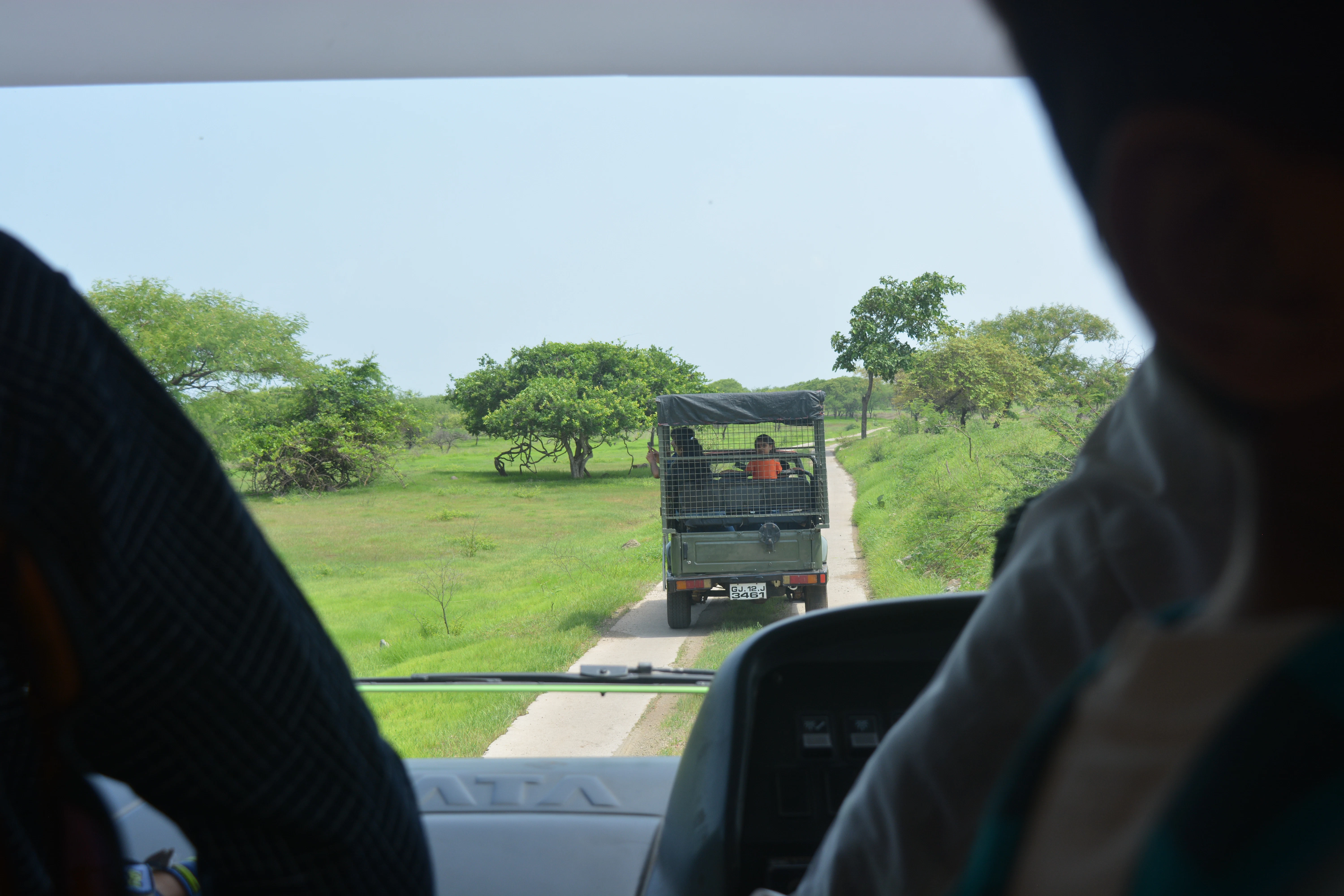Two military trucks drive down a dirt road.