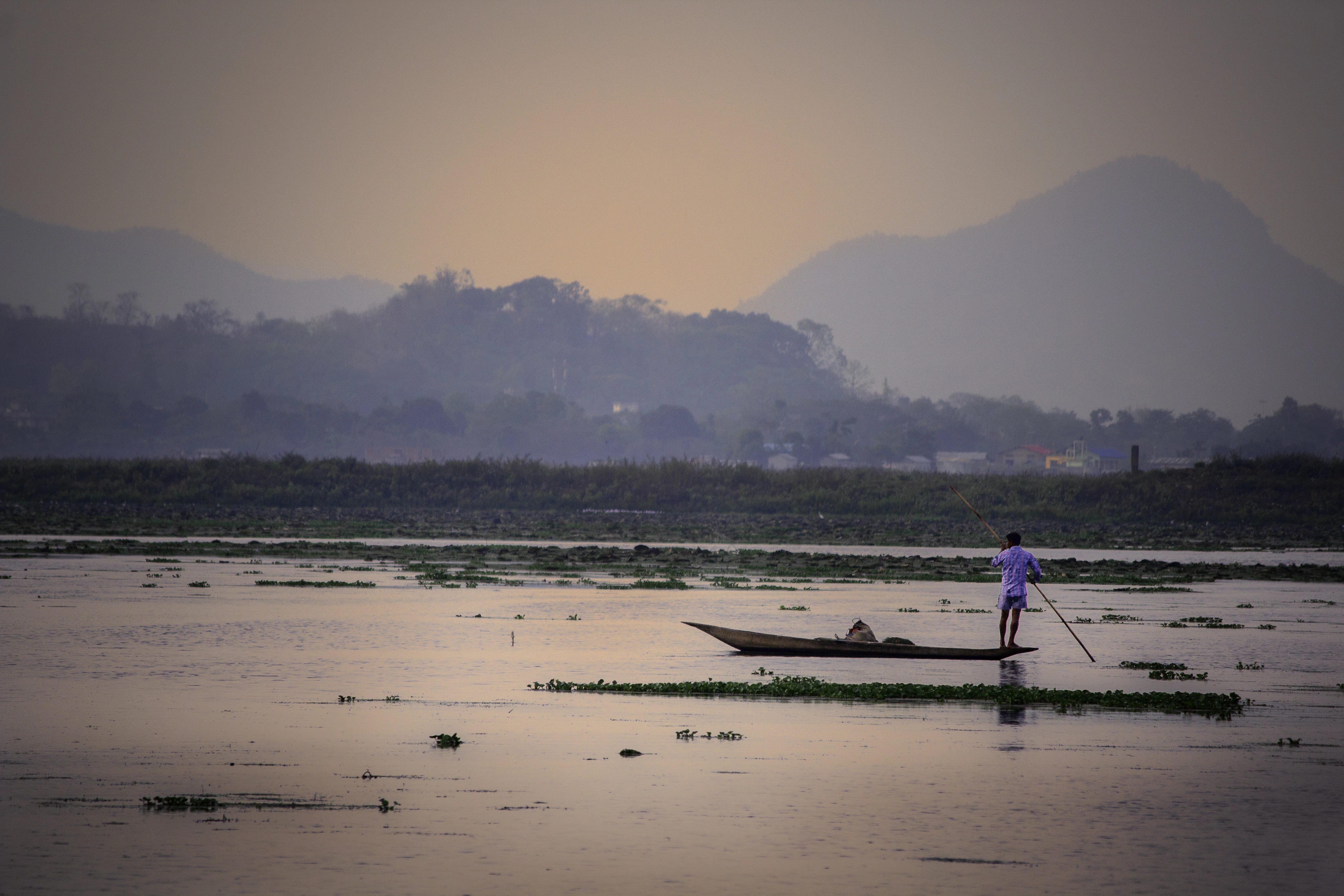 Man rows boat on calm water at sunset