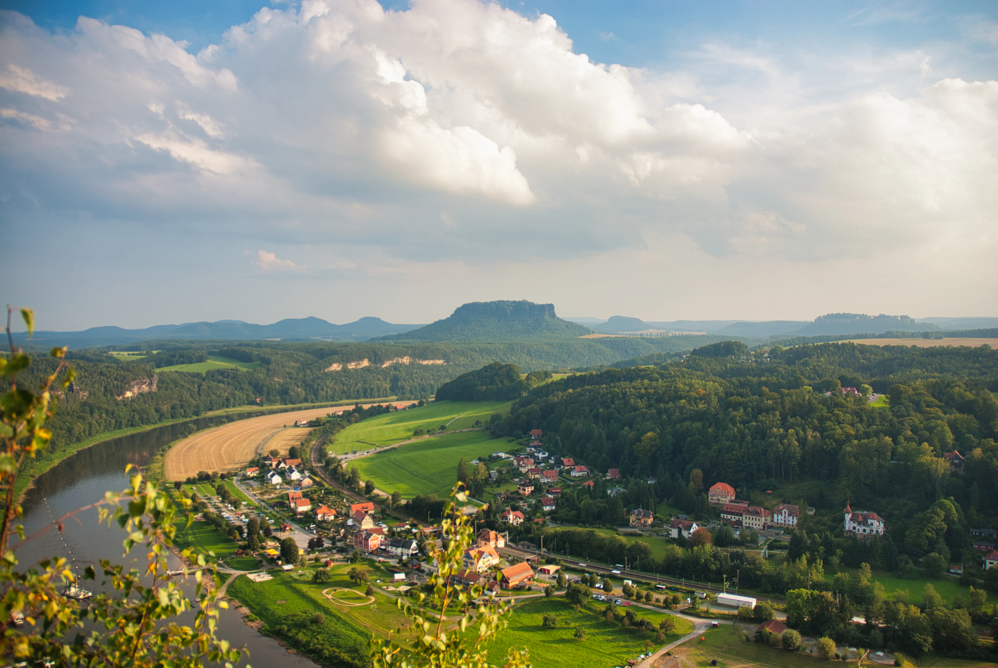 River winds through green valley with village and distant mountains.
