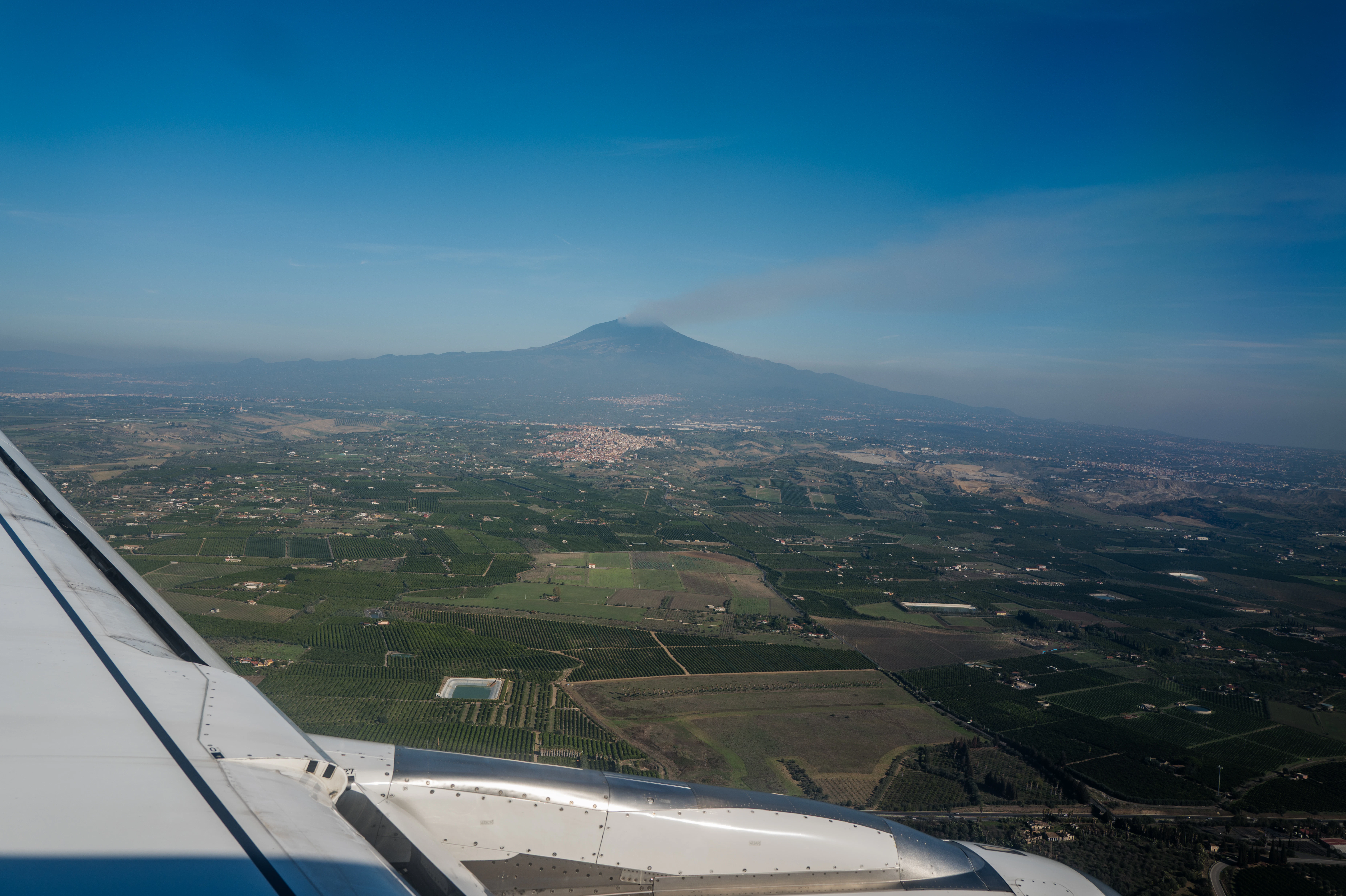 Airplane wing over landscape with distant mountain.