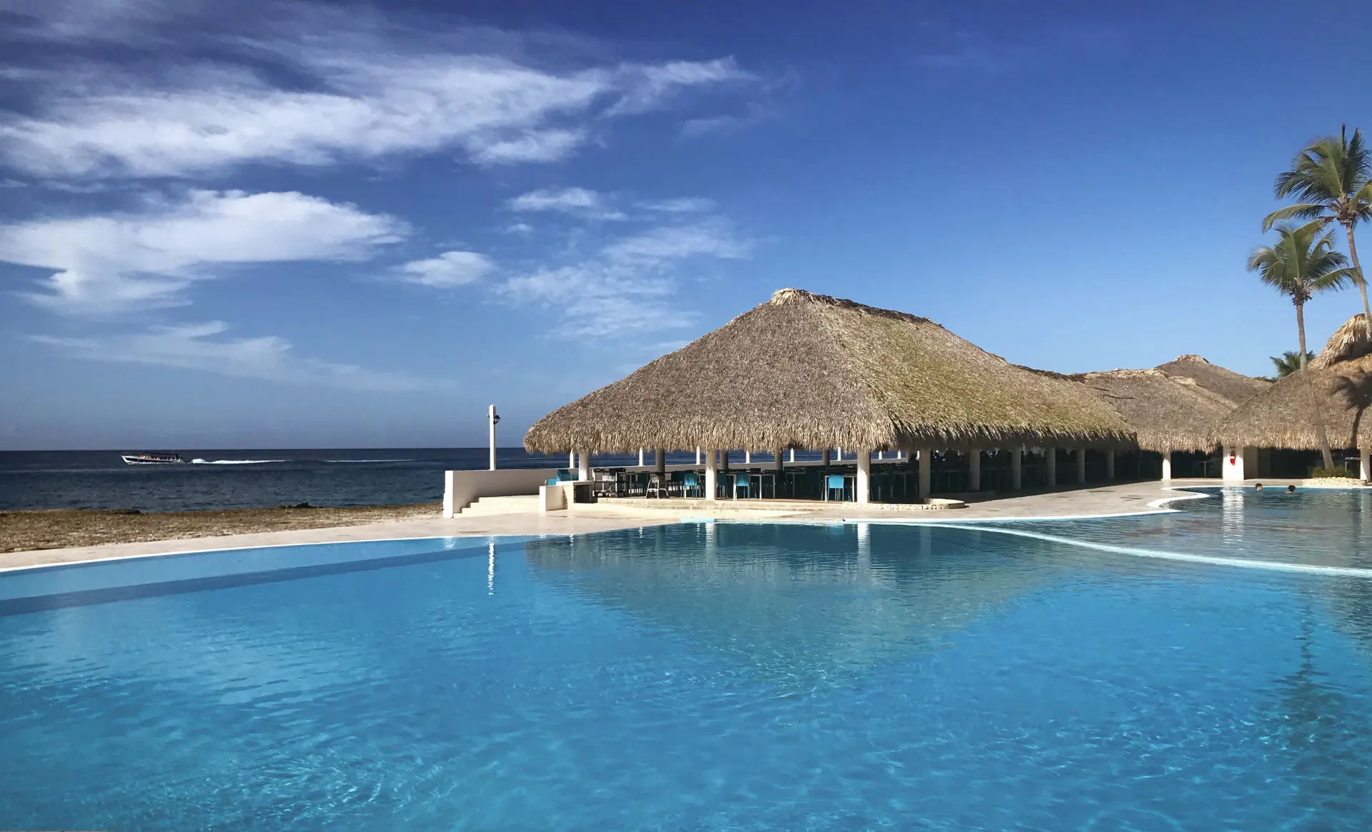 a large pool with a thatched roof next to the ocean