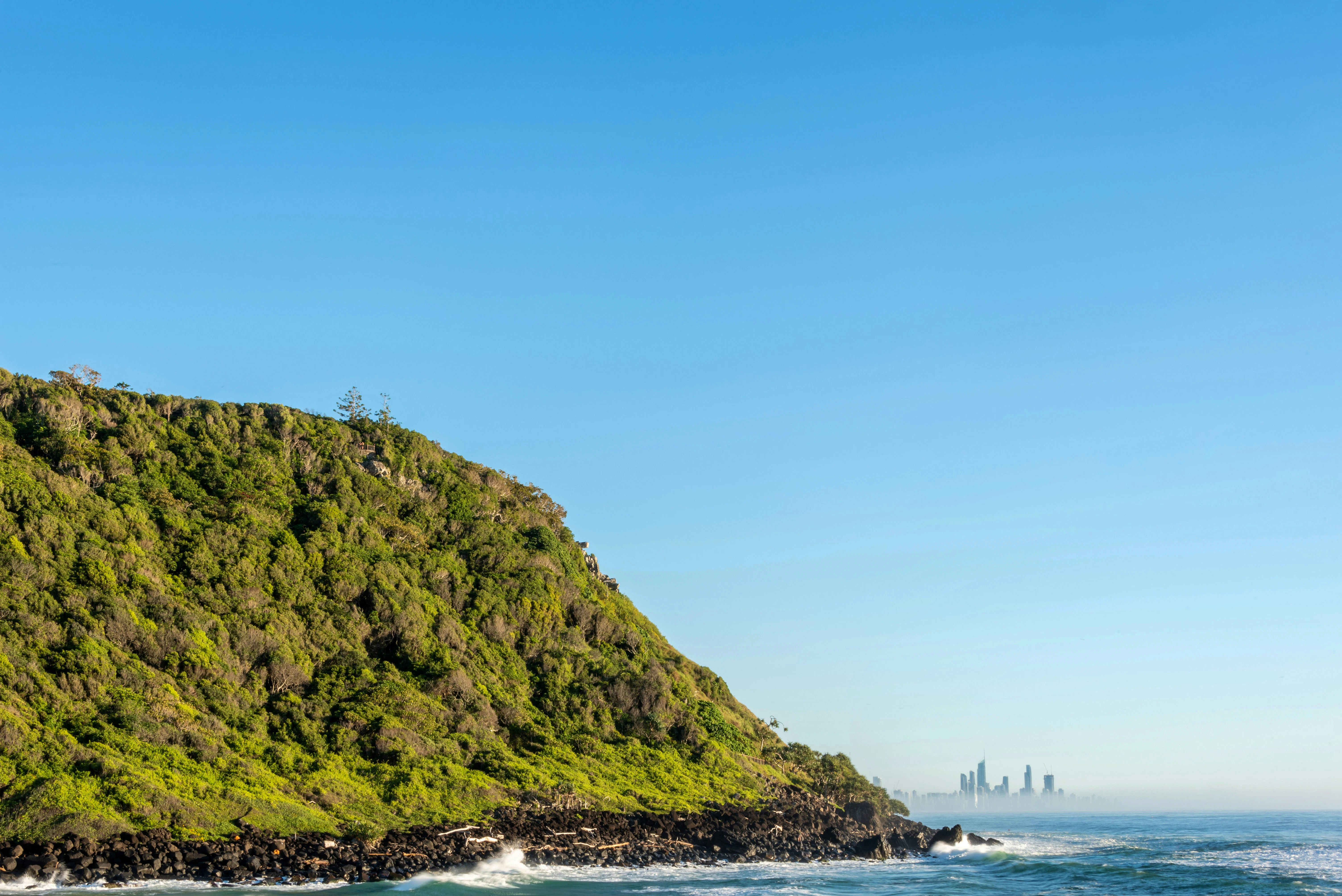 Green cliff overlooking the ocean with distant city skyline