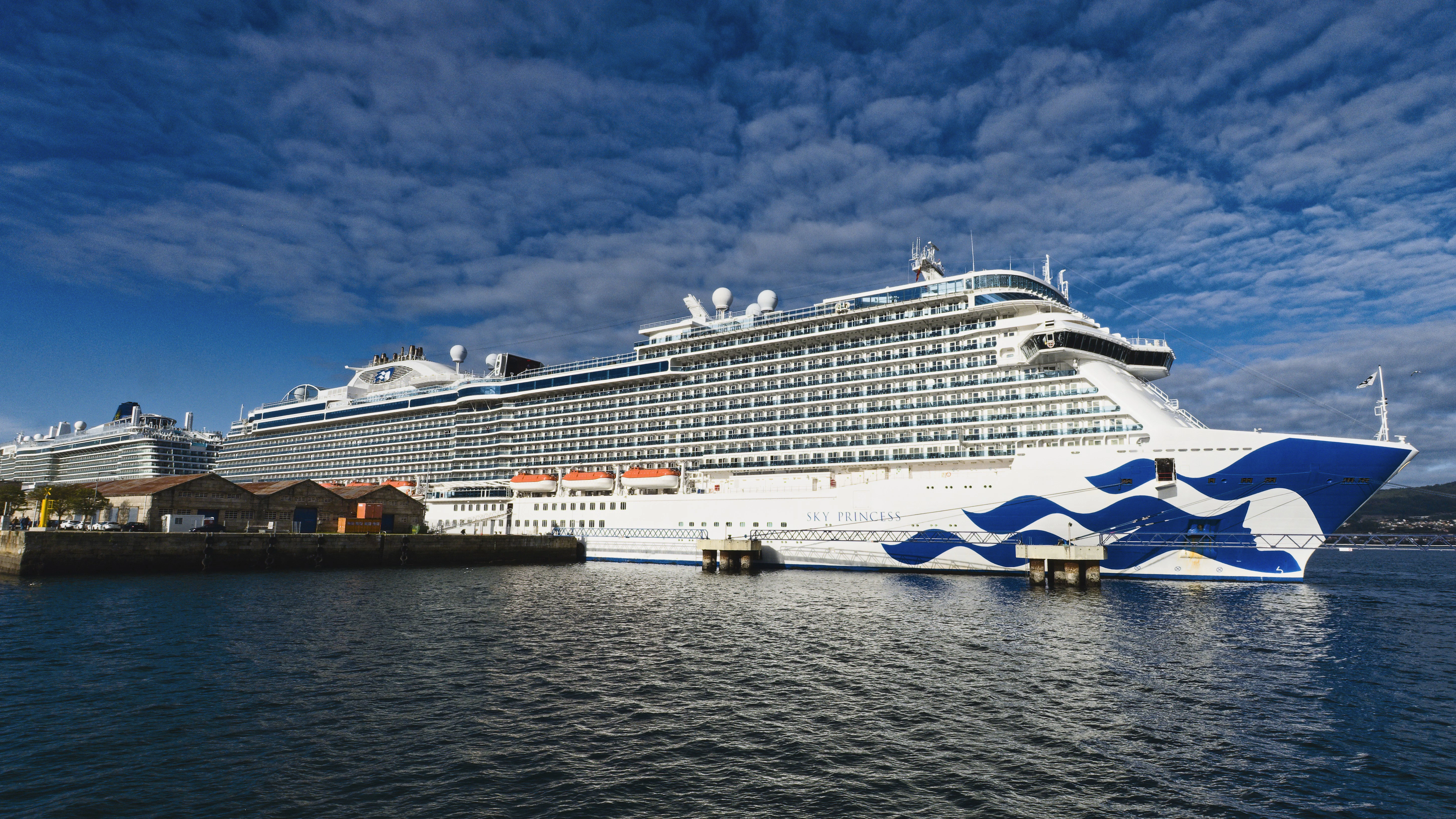 Large white cruise ship docked at harbor under blue sky.
