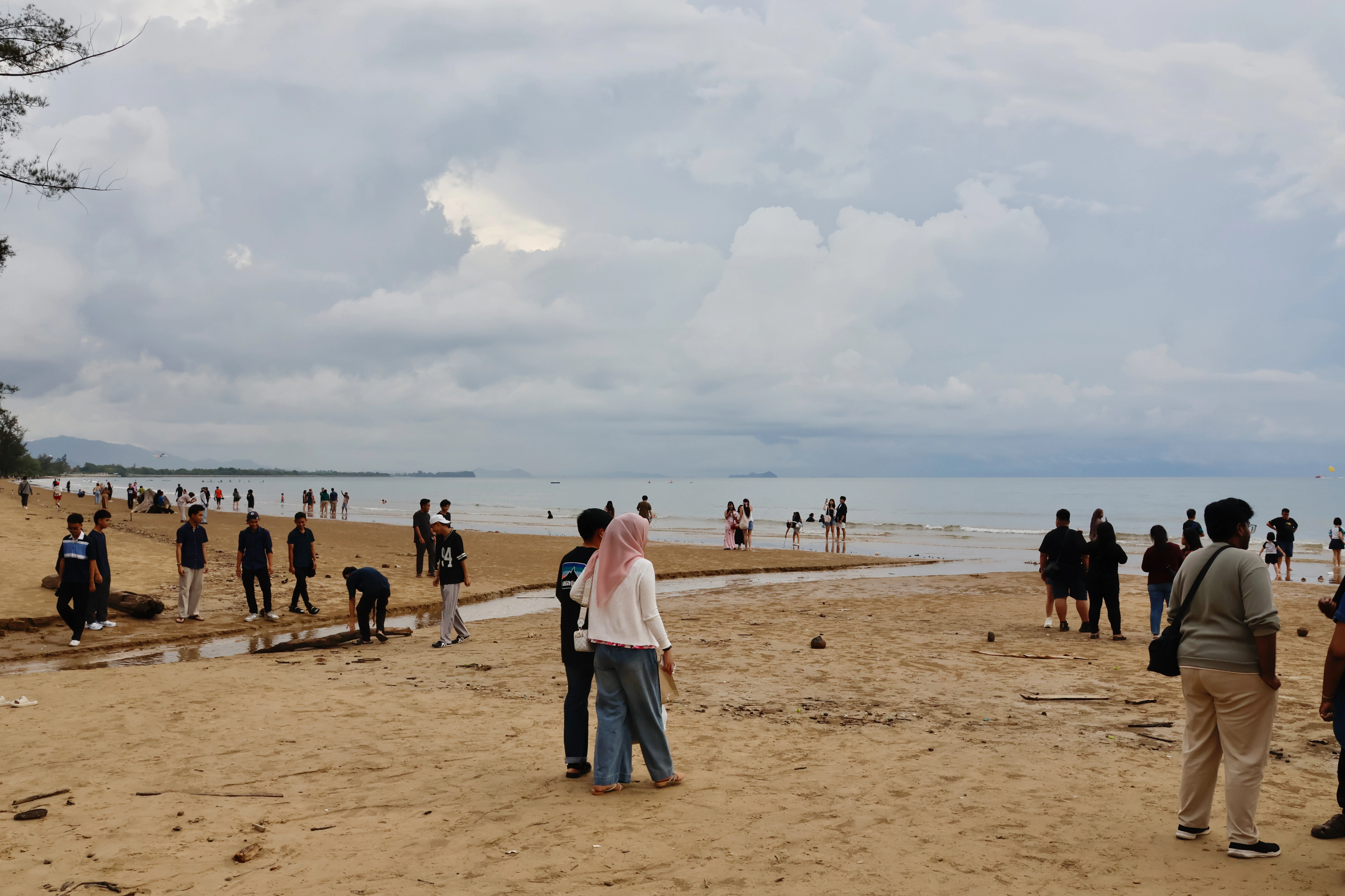 People gathered on a sandy beach under cloudy skies.