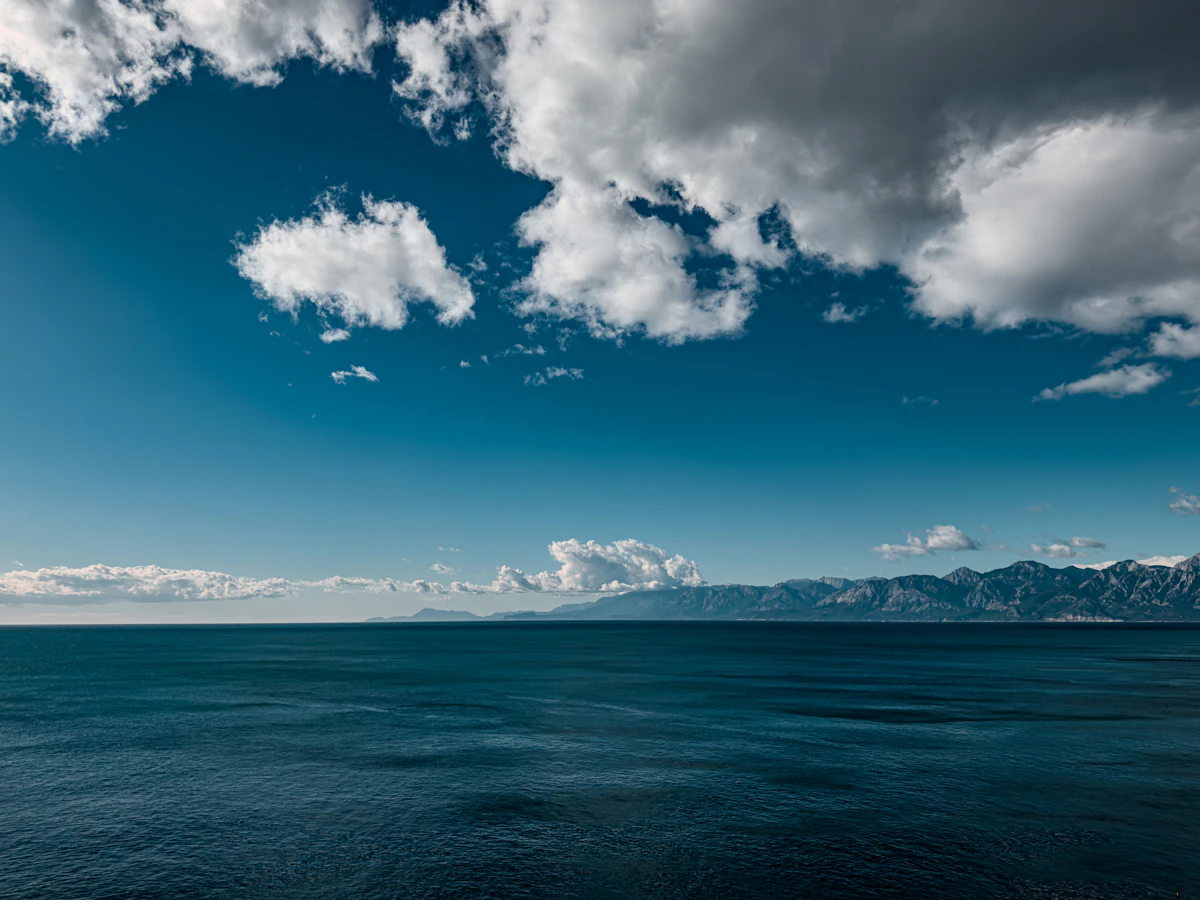 Vast blue ocean meets distant mountains under cloudy sky