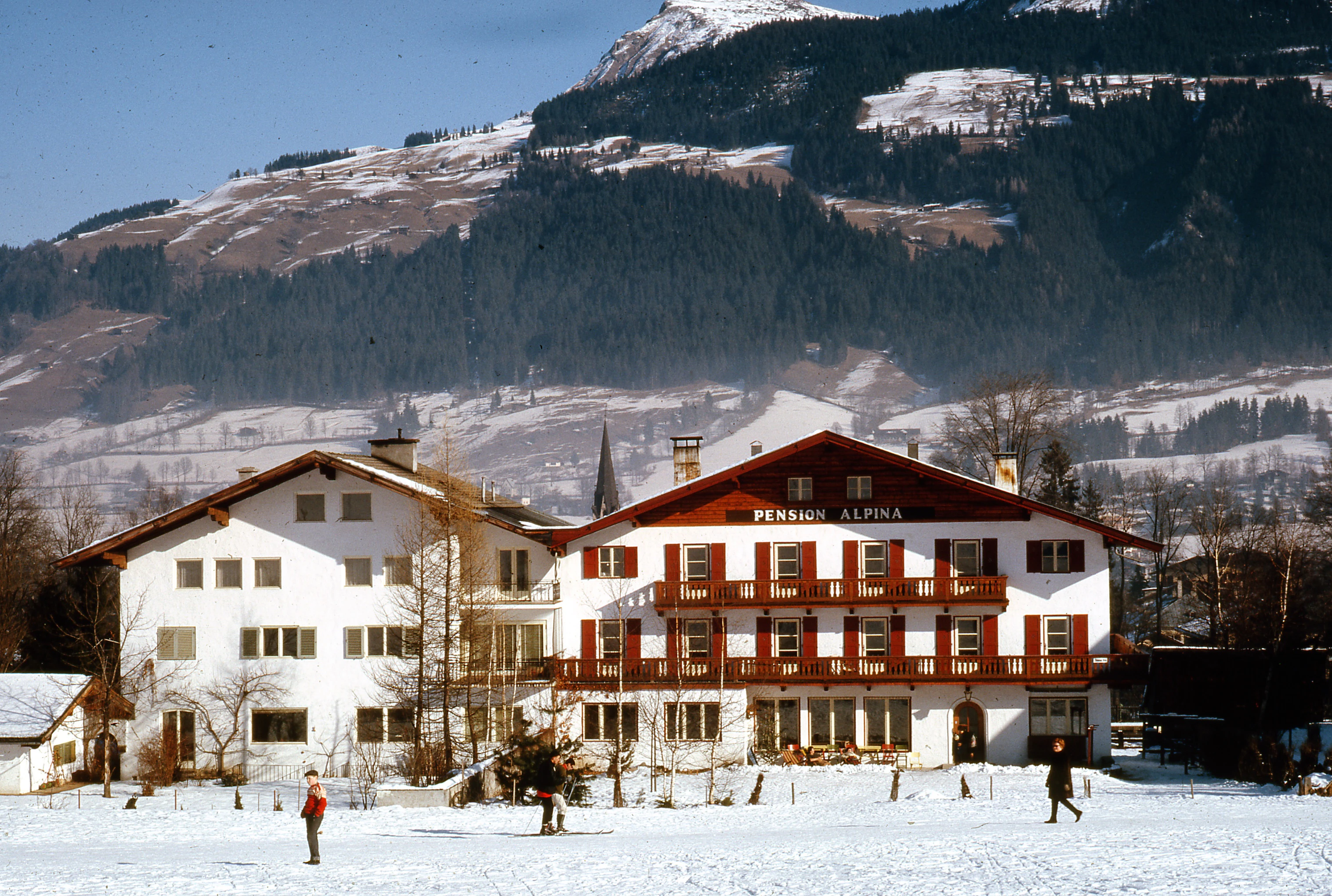 a large white building with red shutters in front of a mountain