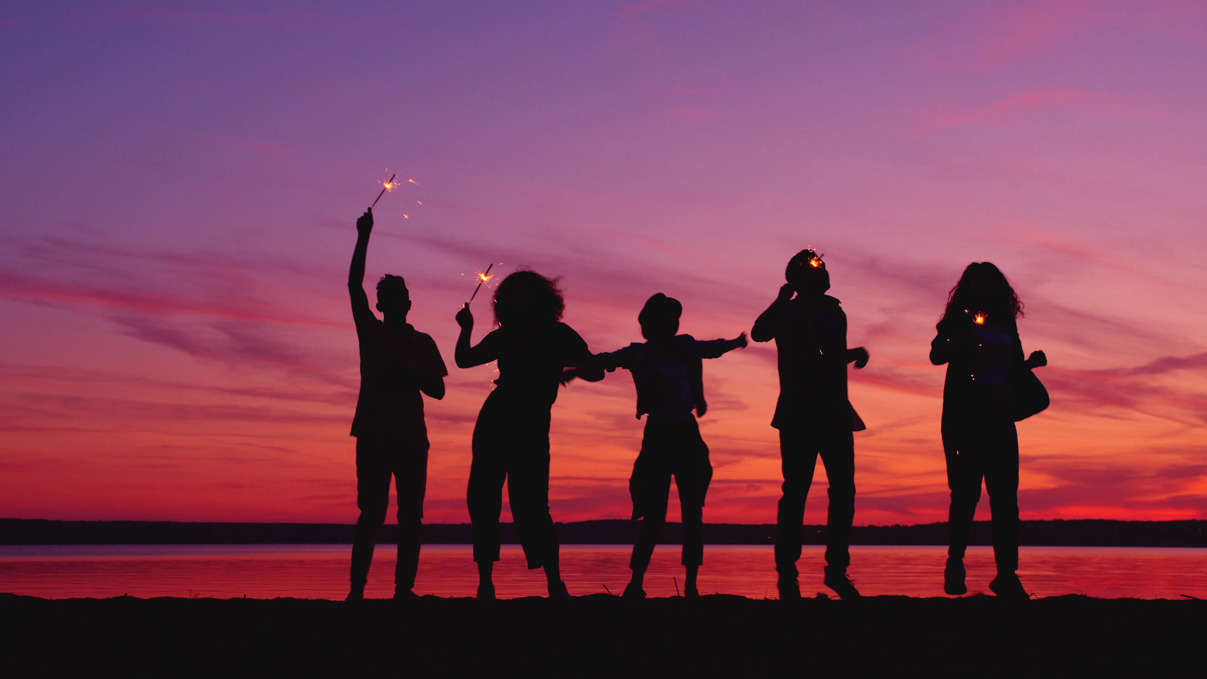 Silhouettes of friends celebrating with sparklers at sunset